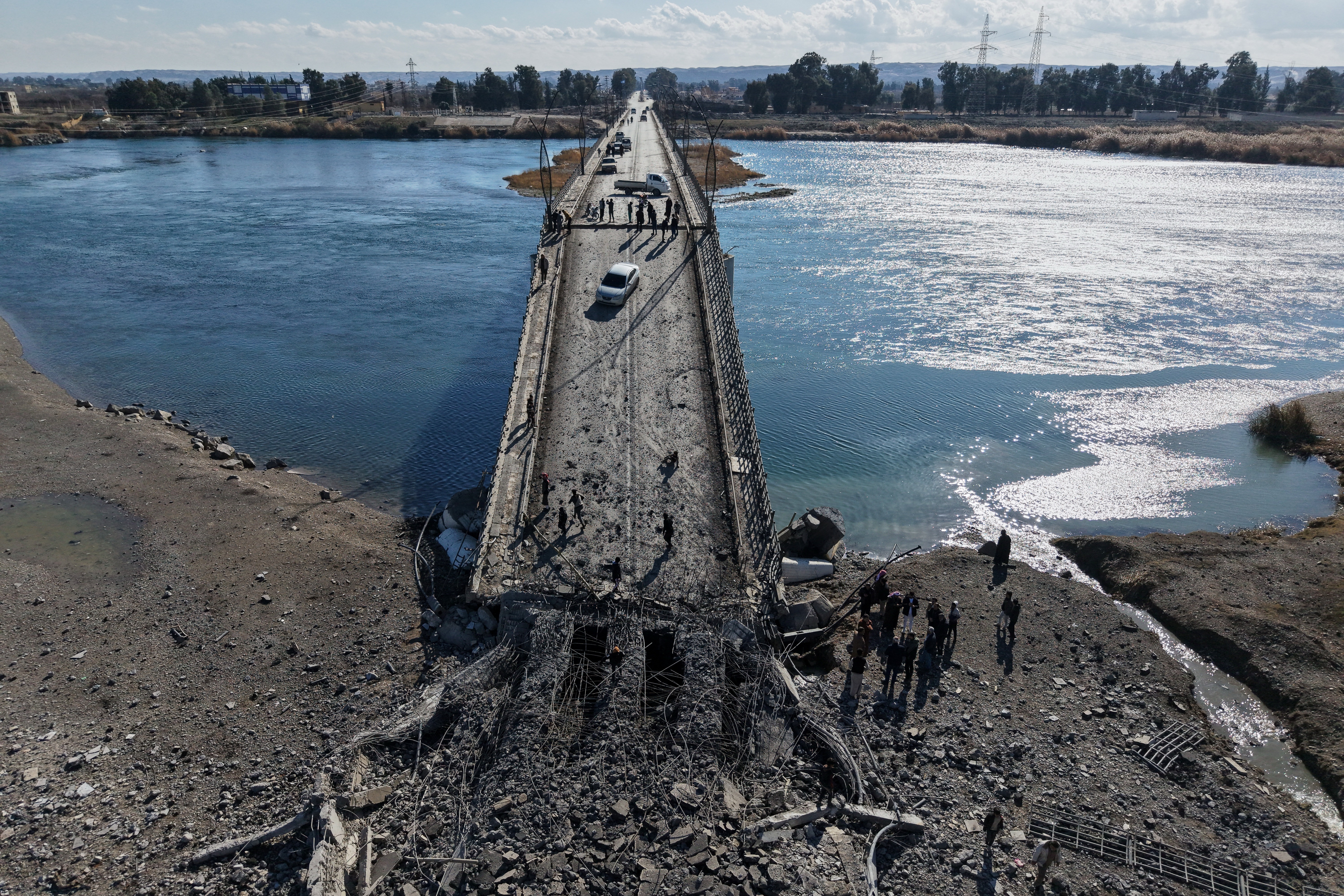 People cross the damaged Al-Rashid Bridge on foot, destroyed by retreating Syrian Democratic Forces (SDF) troops, a day after Syrian government troops took control of the area on the outskirts of Raqqa, northeastern Syria, Monday, Jan. 19, 2026. (AP Photo/Omar Albam)