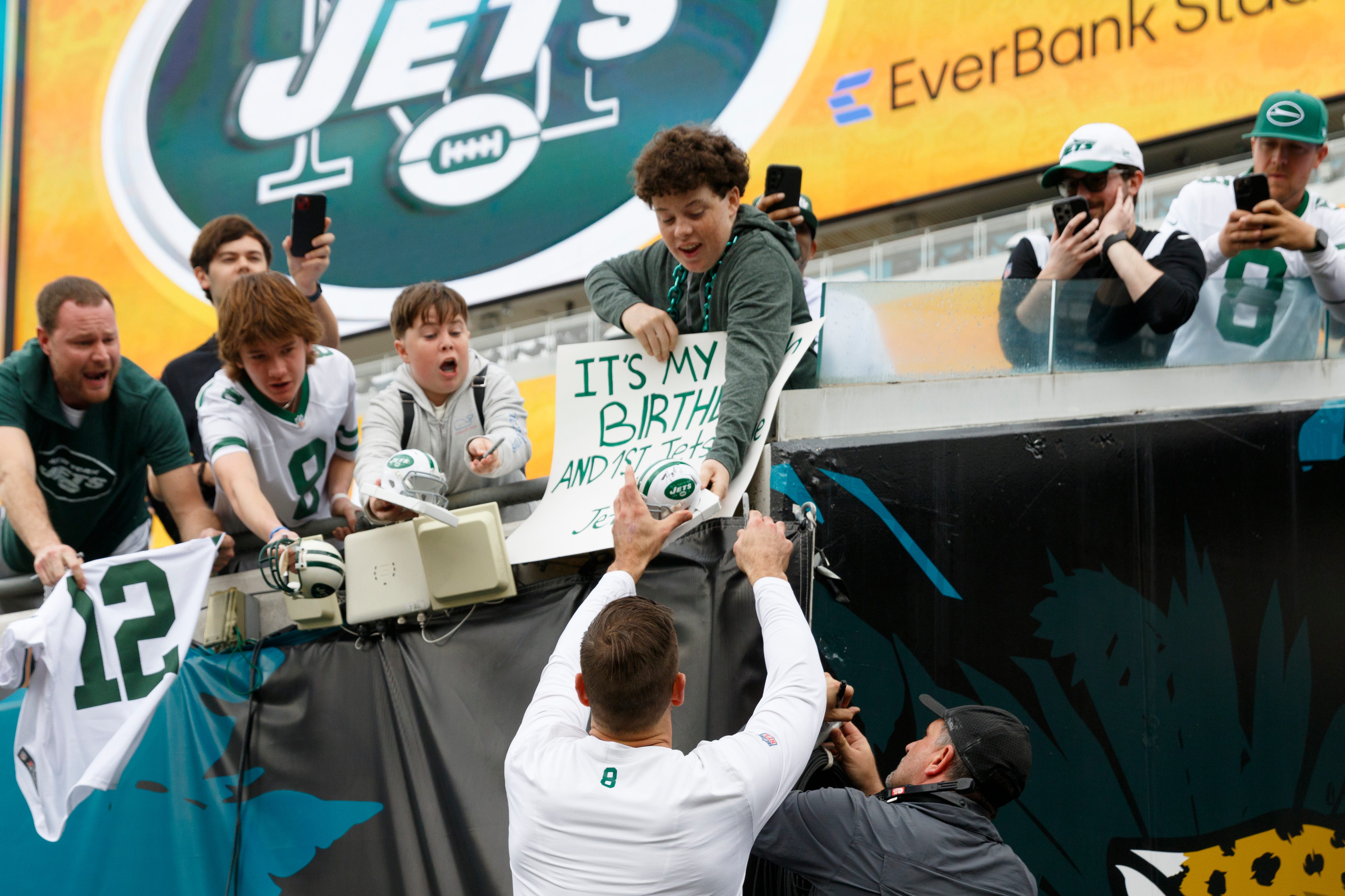 New York Jets quarterback Aaron Rodgers (8) signs a fan's helmet before the game against the Jacksonville Jaguars at EverBank Stadium in Jacksonville, Florida, on Dec. 15, 2024.